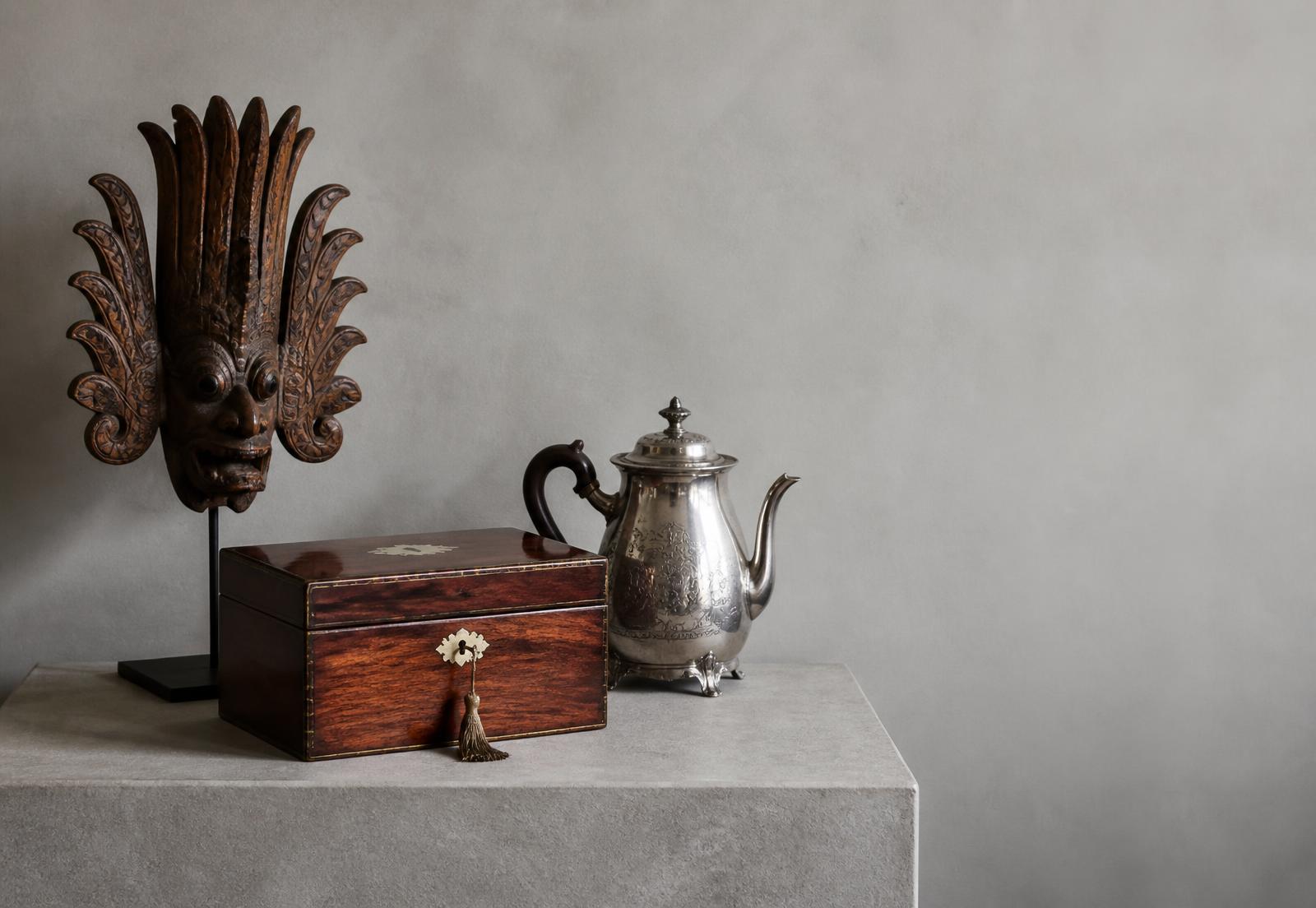 Victorian brass instruments beside Sri Lankan carved wood and lacquerware on a grey studio table